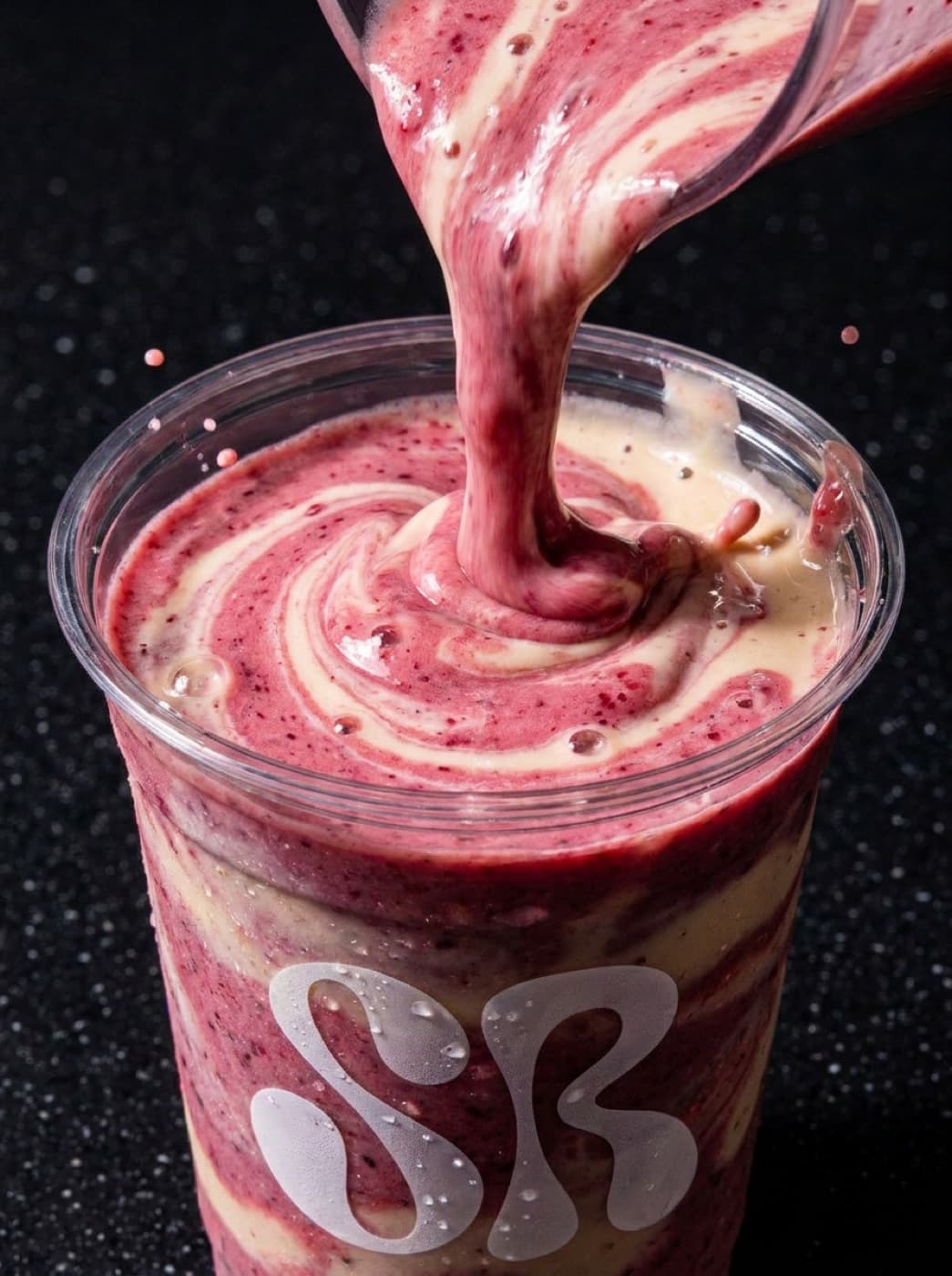 A berry shake being poured into a Shakeroom cup on a dark surface